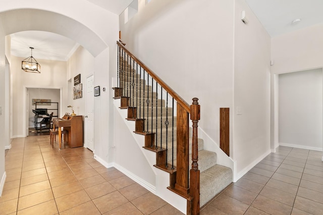 stairway with an inviting chandelier, tile patterned floors, and a towering ceiling