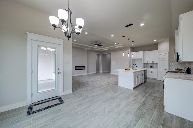 kitchen with sink, a kitchen island with sink, hanging light fixtures, white cabinetry, and decorative backsplash