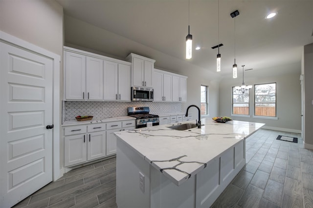 kitchen with stainless steel appliances, a kitchen island with sink, sink, and white cabinets