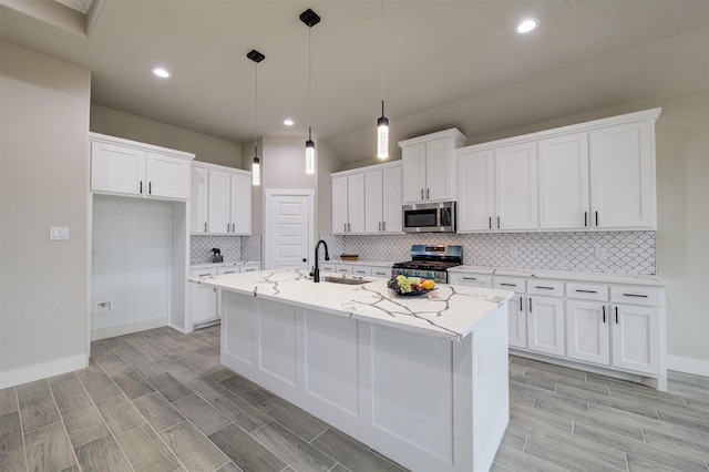 kitchen with appliances with stainless steel finishes, an island with sink, white cabinets, hanging light fixtures, and light stone countertops