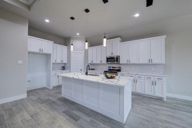 kitchen featuring appliances with stainless steel finishes, decorative light fixtures, white cabinets, light stone counters, and a center island with sink