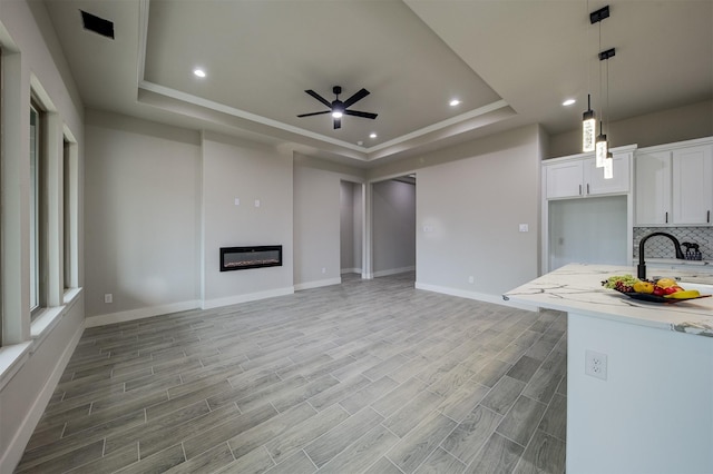 kitchen with tasteful backsplash, a raised ceiling, pendant lighting, ceiling fan, and white cabinets