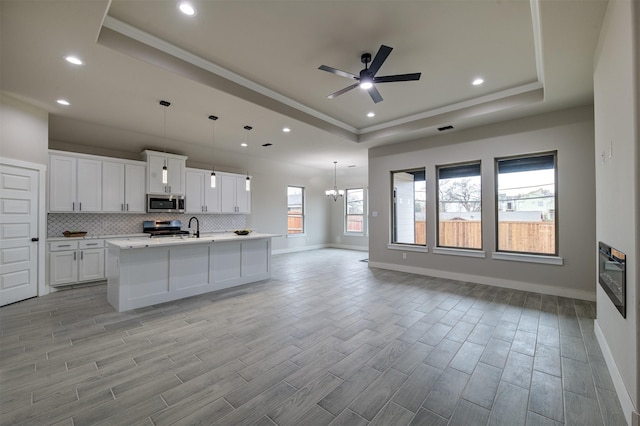 kitchen featuring white cabinetry, appliances with stainless steel finishes, a raised ceiling, and a center island with sink