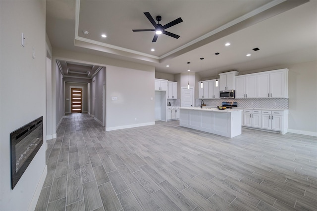 kitchen with stainless steel appliances, a raised ceiling, a center island with sink, and white cabinets