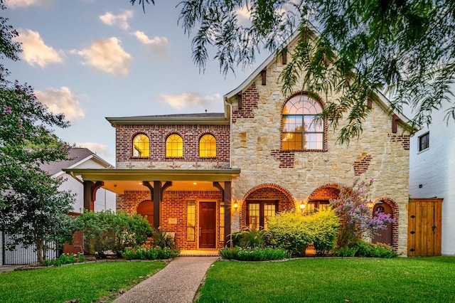 view of front of home with a front yard, stone siding, brick siding, and fence