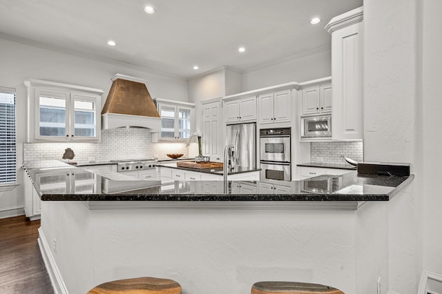 kitchen featuring custom exhaust hood, kitchen peninsula, stainless steel appliances, and white cabinetry