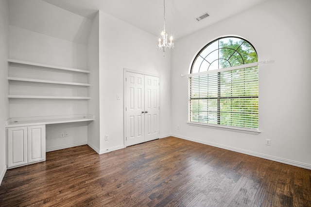 unfurnished bedroom with baseboards, visible vents, built in study area, dark wood-type flooring, and a chandelier