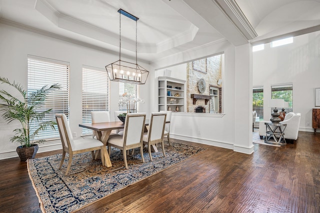 dining room with dark wood-type flooring, ornamental molding, a raised ceiling, and a fireplace