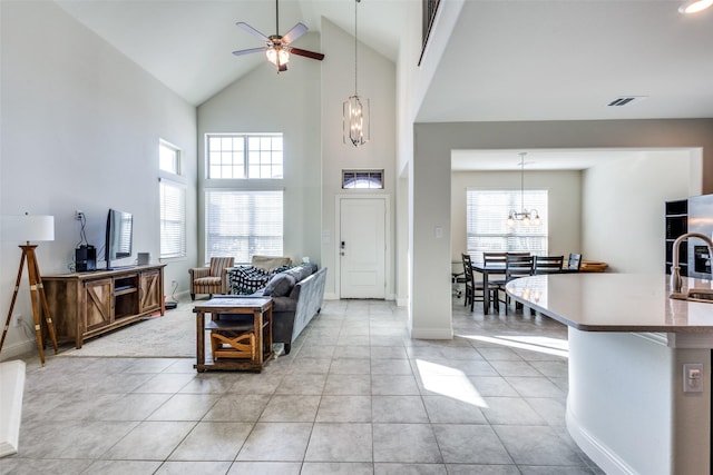 tiled living room with ceiling fan with notable chandelier, a towering ceiling, and sink