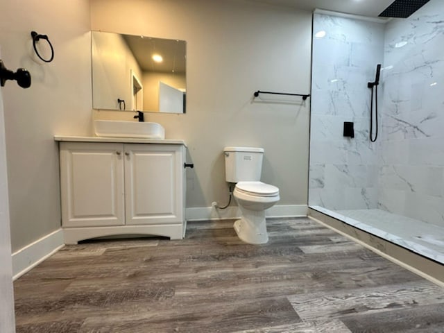 bathroom featuring wood-type flooring, toilet, vanity, and tiled shower