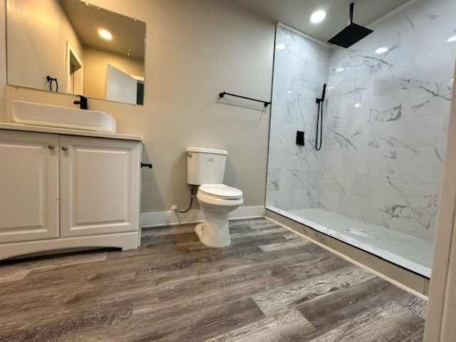 bathroom with vanity, toilet, hardwood / wood-style flooring, and tiled shower