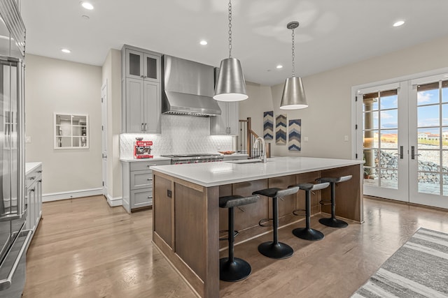 kitchen with pendant lighting, a center island with sink, wall chimney exhaust hood, and french doors