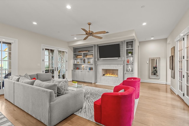 living room featuring light hardwood / wood-style floors, ceiling fan, a fireplace, french doors, and built in shelves