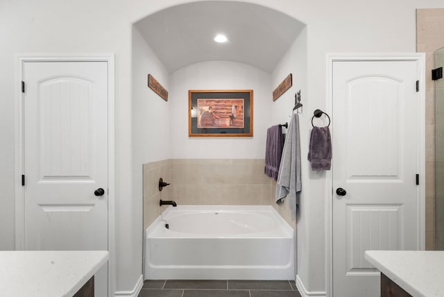 bathroom with a washtub, vanity, lofted ceiling, and tile patterned flooring