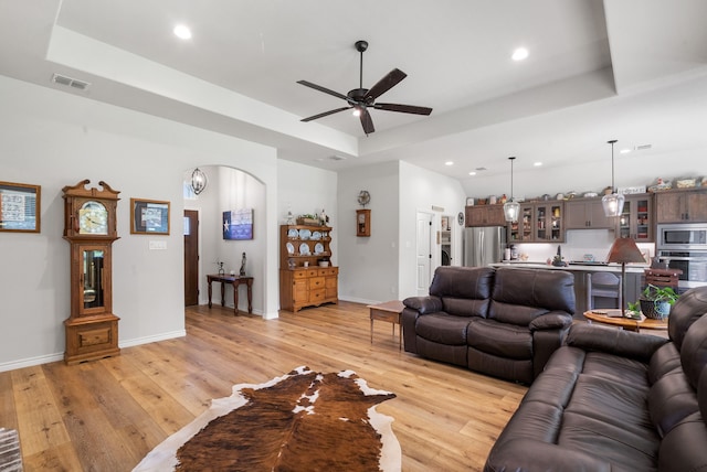 living room featuring ceiling fan, a raised ceiling, and light wood-type flooring