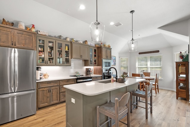 kitchen featuring appliances with stainless steel finishes, sink, backsplash, hanging light fixtures, and a center island with sink