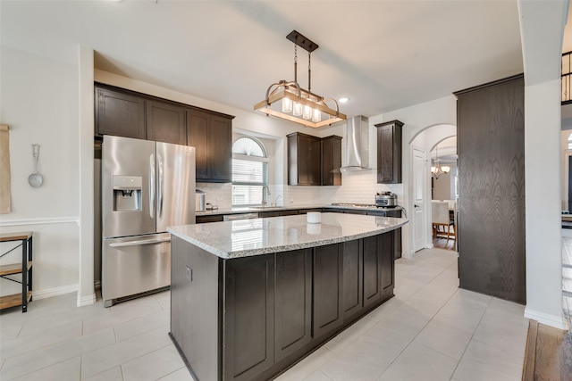 kitchen featuring a kitchen island, stainless steel refrigerator with ice dispenser, sink, light stone countertops, and wall chimney exhaust hood