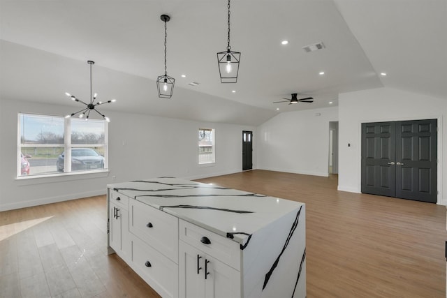 kitchen featuring white cabinetry, light wood-type flooring, hanging light fixtures, vaulted ceiling, and light stone counters