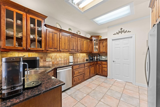 kitchen with stainless steel appliances, tasteful backsplash, dark stone countertops, sink, and light tile patterned flooring