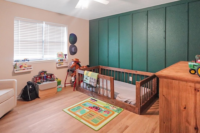 bedroom featuring ceiling fan, a nursery area, and light wood-type flooring