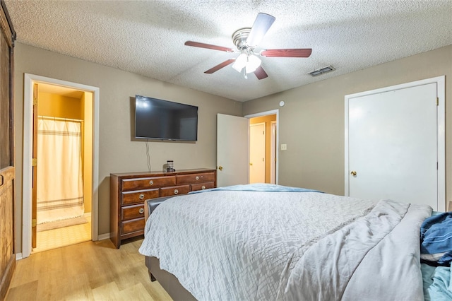 bedroom featuring ceiling fan, a textured ceiling, light hardwood / wood-style flooring, and ensuite bath