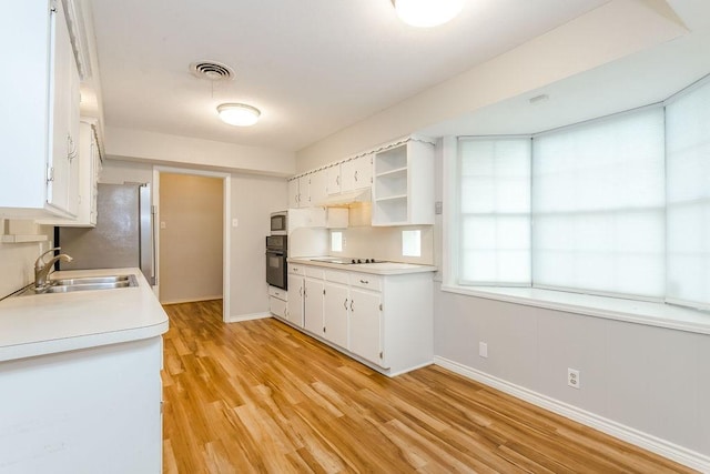 kitchen with sink, white cabinetry, black appliances, and light hardwood / wood-style flooring