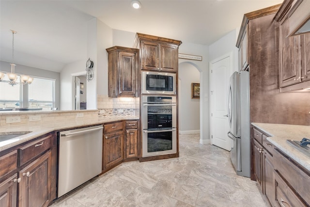 kitchen featuring pendant lighting, stainless steel appliances, tasteful backsplash, a chandelier, and light stone counters