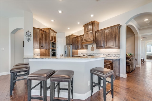 kitchen with kitchen peninsula, appliances with stainless steel finishes, decorative backsplash, dark wood-type flooring, and light stone countertops