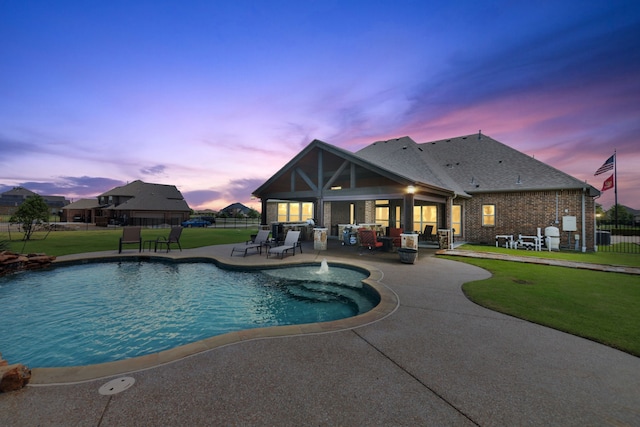 pool at dusk featuring a patio area and a lawn