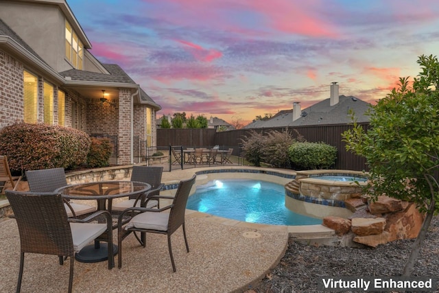 pool at dusk featuring an in ground hot tub and a patio