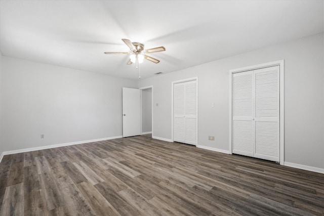 unfurnished bedroom with ceiling fan, two closets, and dark hardwood / wood-style floors