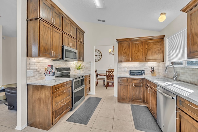 kitchen featuring vaulted ceiling, decorative backsplash, stainless steel appliances, light tile patterned floors, and light stone counters