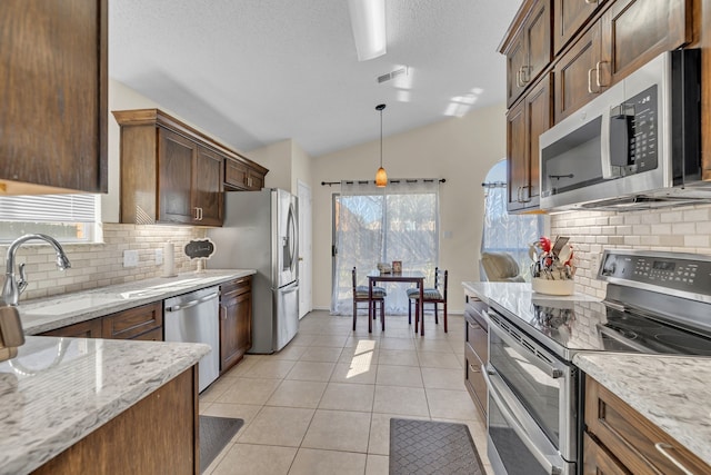 kitchen featuring decorative light fixtures, vaulted ceiling, appliances with stainless steel finishes, light stone countertops, and light tile patterned floors