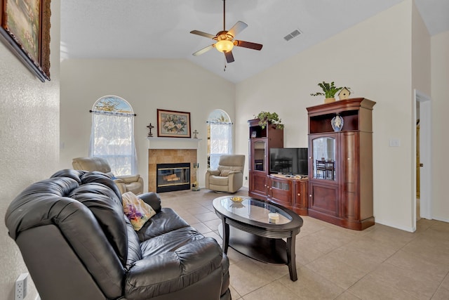 tiled living room with ceiling fan, vaulted ceiling, and a tiled fireplace