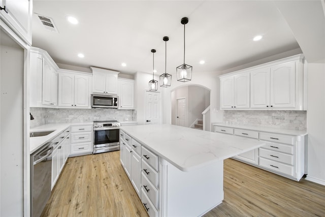 kitchen with hanging light fixtures, white cabinets, stainless steel appliances, and a kitchen island