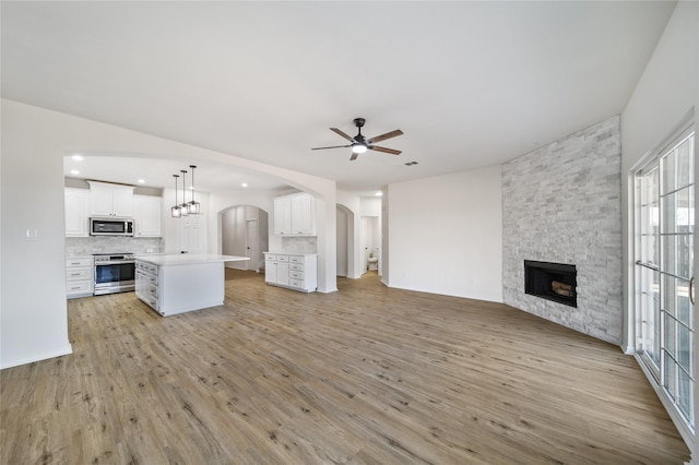 unfurnished living room with ceiling fan, a fireplace, and light hardwood / wood-style flooring