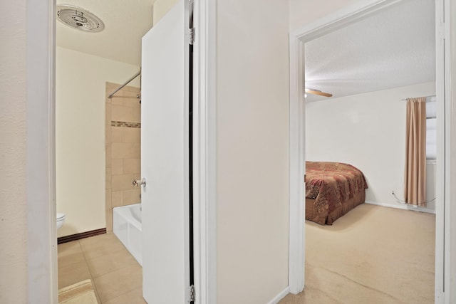 bathroom with a textured ceiling, tiled shower / bath combo, toilet, and tile patterned flooring