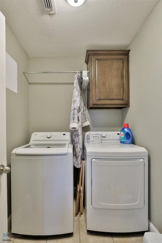 laundry room featuring a textured ceiling, cabinets, light tile patterned flooring, and independent washer and dryer