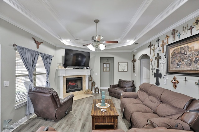 living room with a fireplace, light wood-type flooring, ceiling fan, a tray ceiling, and crown molding