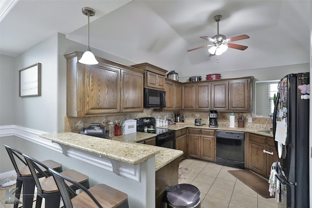 kitchen featuring light stone counters, a breakfast bar, black appliances, and tasteful backsplash