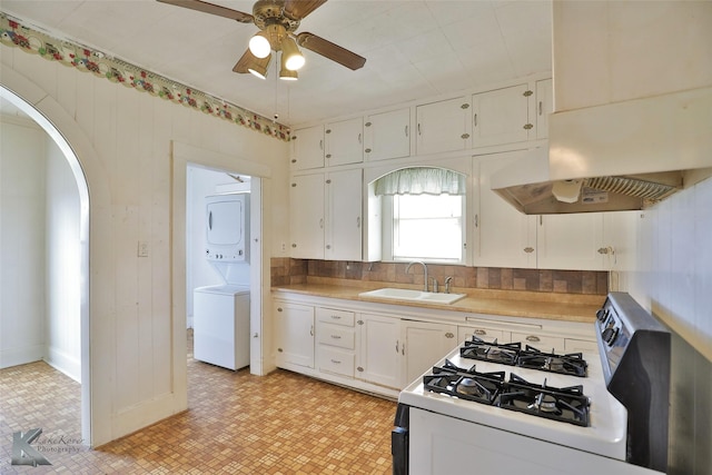 kitchen featuring gas range gas stove, sink, stacked washing maching and dryer, white cabinets, and ventilation hood