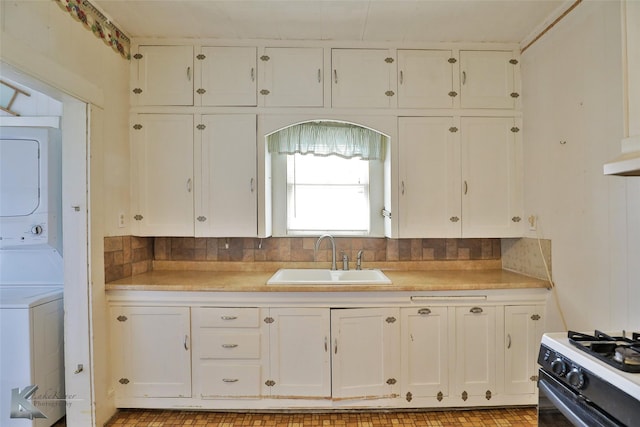 kitchen featuring range with gas cooktop, white cabinetry, tasteful backsplash, sink, and stacked washer and clothes dryer