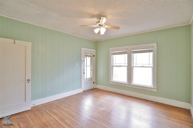 spare room with a textured ceiling, ceiling fan, light hardwood / wood-style floors, and wood walls