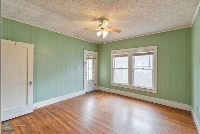 unfurnished room with ceiling fan, wood walls, crown molding, light wood-type flooring, and a textured ceiling