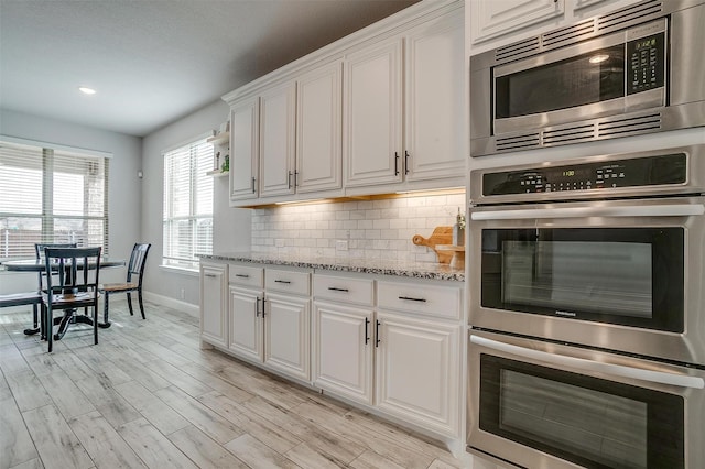 kitchen featuring light hardwood / wood-style floors, stainless steel appliances, decorative backsplash, white cabinets, and light stone counters