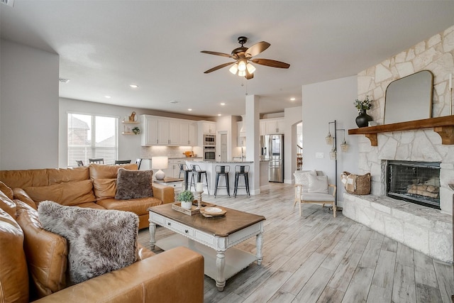 living room featuring light wood-type flooring, visible vents, a fireplace, and ceiling fan