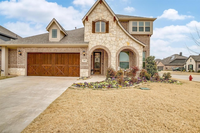 view of front of property featuring a garage, a shingled roof, concrete driveway, stone siding, and brick siding