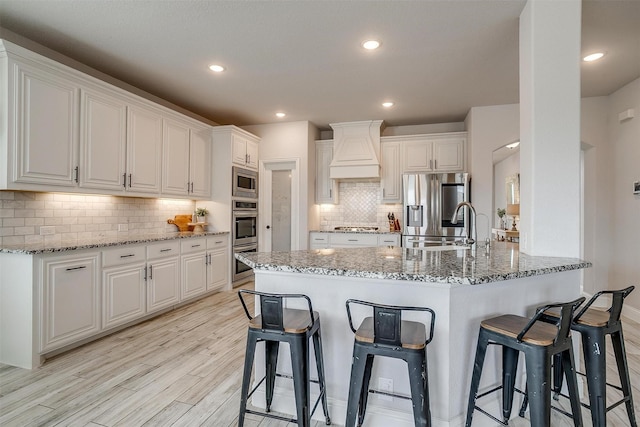 kitchen featuring stainless steel appliances, premium range hood, a peninsula, white cabinetry, and light wood-style floors