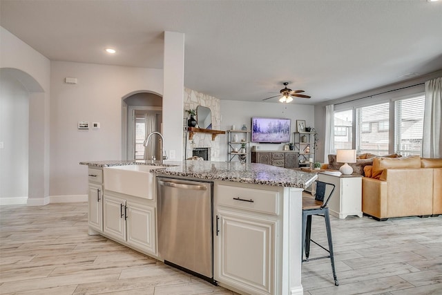 kitchen with a kitchen island with sink, arched walkways, open floor plan, and stainless steel dishwasher