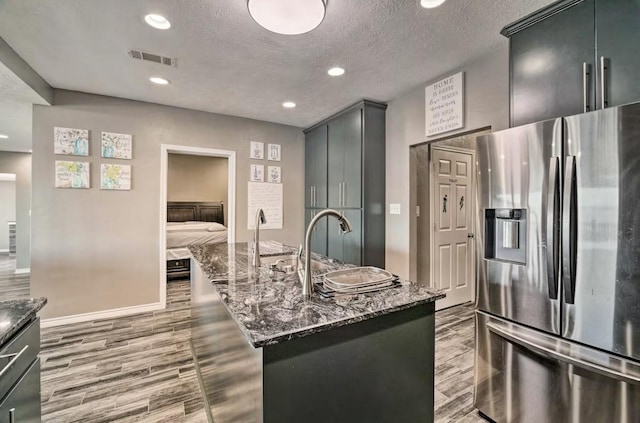 kitchen with stainless steel fridge with ice dispenser, a textured ceiling, a kitchen island, and dark stone countertops